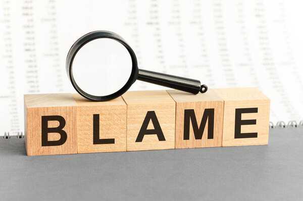 Wooden Blocks with the text: blame with magnifying glass. blame word made with building blocks. Business concept
