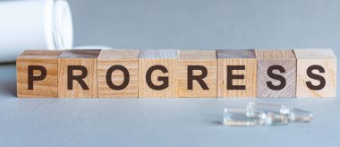Tahta bloklar üzerinde PROGRESS metni. Bir sıra küpün önünde ampuller, arka planda - tabletlerden alınan beyaz plastik ambalajlar, gri bir yüzey üzerinde yer almaktadır. Resmi Kabul Et