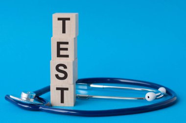 Tahta bloklar ve steteskop üzerine yazılmış test sözcükleri açık mavi arka plan, sigorta ve tıbbi konsept