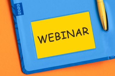 Webinar kelimesi sarı not kağıdına siyah harflerle yazılmıştır. Mavi günlüğün arka planında sarı bir kalem gömülü..