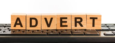 Yapı taşlarından yapılmış bir kelime. Siyah yazı tipiyle yazılmış bir sıra tahta küp siyah bir klavyede yer almaktadır..