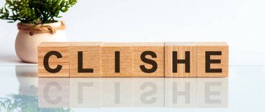 Clishe - eğimli bir arkaplanda tahta küplerin üzerine metin. CLIHE kelimesi siyah harflerle yazılır ve masanın ayna yüzeyine yansıtılır. Ön görüş kavramları, arka planda çiçekler.