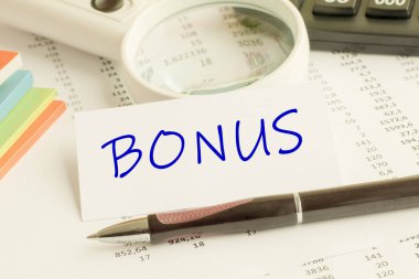 Beyaz kağıtta açık beyaz fon üzerine bonus metin. Arka planda bir büyüteç, bir diyagram, bir hesap makinesi ve üzerinde numaralar olan bir kalem var..