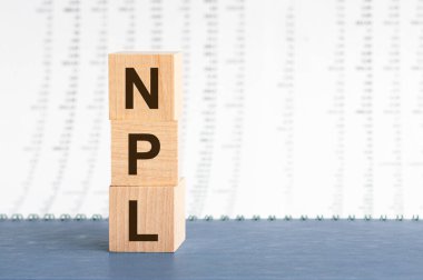 Sayı sütunlarının arkaplanındaki tahta blokların dikey sırasına NPL yaz. NPL - Performans Olmayan Krediler - Gri masadaki tahta küplere kısaltma, iş konsepti geçmişi