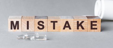 Hata, ahşap küplere siyah harflerle yazılmış bir kelimedir, gri arka plan. Tahta bloklardaki hata metni. Küplerin önünde ampuller, arkaplan - tabletlerden alınan beyaz plastik ambalaj.