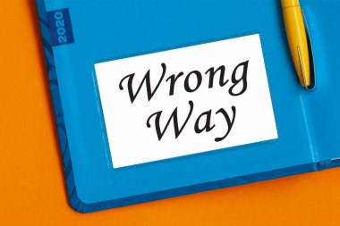 Yanlış yol, kağıt üzerinde kelime. Günlük planlamacıdan gelen beyaz kartvizitteki yanlış kelimeler. Mavi günlük ve sarı kalem turuncu masada..