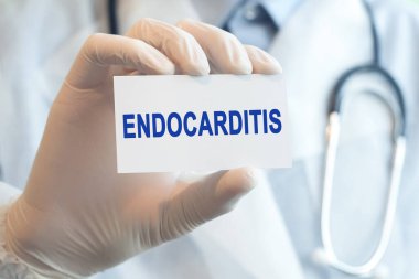 Doktor elinde beyaz kağıt bir kart tutuyor. İçinde ENDOCARDITIS yazıyor. Tıbbi konsept. Tıp doktorunun elinde Endokardit kartı var. Hastane, klinik ve tıbbi otobüsler için sağlık hizmetleri kavramı.