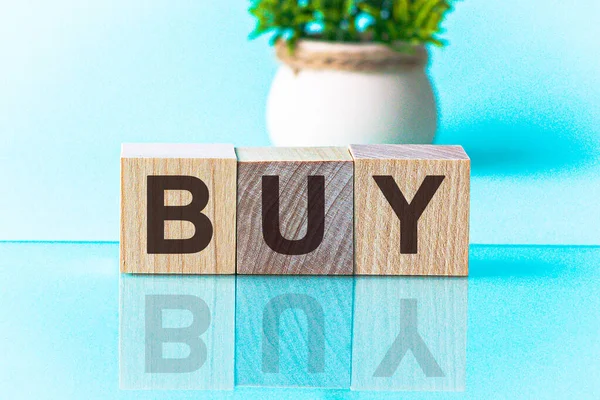 BUY word written on wood block. BUY - word is made of wooden building blocks lying on the yellow table. BUY, marketing concept, blue background