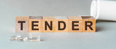 İhale, ahşap küplere siyah harflerle yazılmış, gri arkaplan. Tahta bloklarda nazik metin. Küplerin önünde ampuller, arkaplan - tabletlerden alınan beyaz plastik ambalaj.