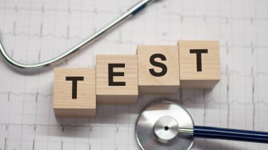 Tahta bloklara ve arka planda steteskopa yazılmış test sözcüğü. Hastane, klinik ve tıbbi otobüsler için sağlık hizmetleri kavramı.