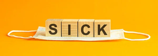 病気という言葉は白い医療面マスクの上に横たわる木製の立方体に書かれています黄色の背景概念 — ストック写真
