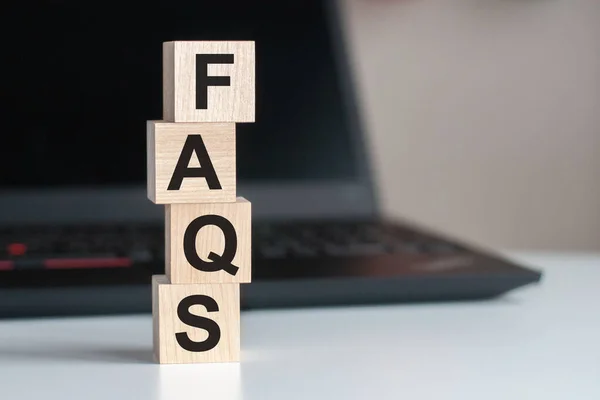 FAQS Frequently asked questions text written on wooden block on computer keyboard against black background. Service support or assitance concept.