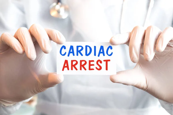 Doctor holding a card with text CARDIAC ARREST in both hands. Medical concept