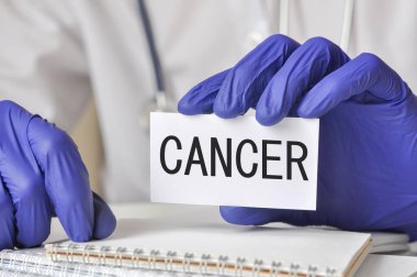 Küçük kartla mavi eldiven verin. Kanser kelimesi beyaz bir sağlık kartıyla yazılmış. Tıbbi konsept.