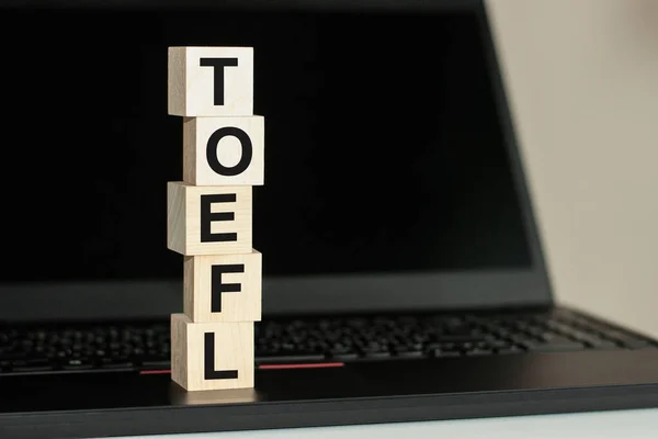 TOEFL - short for Test of English as a Foreign Language - text written on wooden block on computer keyboard against black background. Education concept.