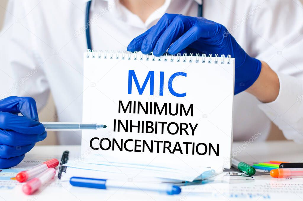 Doctor holding a card with text MIC - short for Minimum Inhibitory Concentration, medical concept. The text is written in blue fnd black letters in a medical journal.