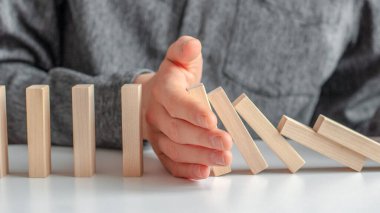 Erkek eli, kahverengi beyaz arka planda domino etkisini durdurdu. Domino etkisi kavramı, zincirleme reaksiyon, risk yönetimi, kopyalama alanı.