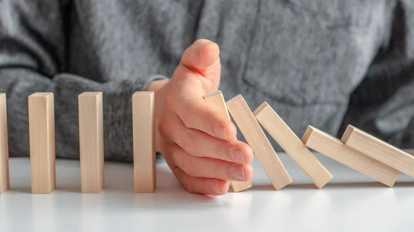 Men\'s hand stopped domino effect, on a brown white background. Concept of domino effect, chain reaction, risk management, copy space.