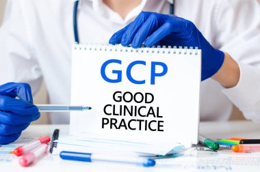 Doktor elinde GCP yazılı bir kart tutuyor. İyi klişe pratiğin kısaltması. Tıbbi konsept. Metin mavi harflerle yazılmış ve tıp dergisinde siyah harfler var..