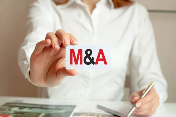 Mergers and Acquisitions message on the card shown by a woman. A woman in a white shirt holds a piece of paper with the text: M and A. Business concept for companies.
