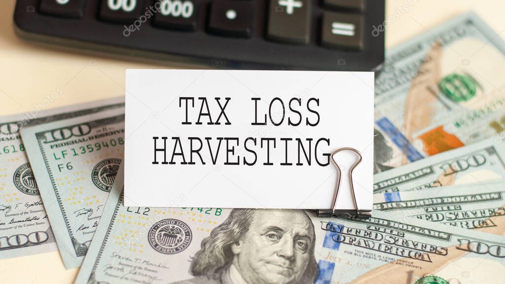 the words TAX LOSS HARVESTING is written on the white card. Card on the background of 100 dollar bills and calculator