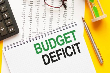Bütçe açığını gösteren metin yazılıyor. Beyaz kart, yeşil ve siyah harfler, sarı arkaplan üzerine metin bütçe DEFICIT yazmak. İş konsepti.