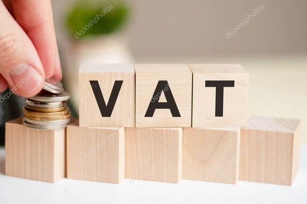 Concept word VAT on wooden blocks on background from green flower. The word VAT on wood cubes with coins and calculator on the background. Business concept. VAT - Value Added Tax