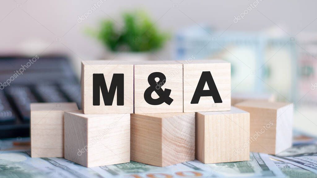 Concept word M and A on wooden blocks on beautiful background from green flower. The word M AND A on wood cubes with coins and calculator on the background. Business concept
