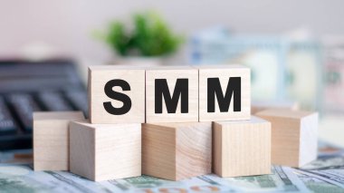 Tahta bloklardaki SMM sözcüğü yeşil çiçeğin güzel arka planında. Arkaplanda para ve hesap makinesi olan tahta küplere SMM kelimesi. İş konsepti. SMM - Sosyal medya pazarlaması