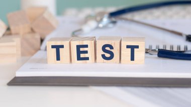 Test kelimesi, kağıt arka planda steteskopun yanındaki tahta küplere yazılır. Tıbbi konsept.