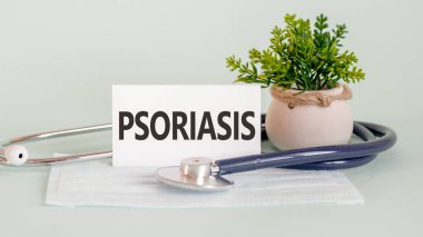 İlaç maskesi, steteskop ve arka planda yeşil çiçek ile beyaz tıp kartı üzerine yazılmış PSORIASIS kelimeleri