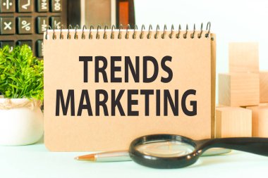 Not defterinde notlar, hesap makinesi, büyüteç, çizelge arkaplanındaki woden bloklar için beyaz kâğıtlardan oluşan TRENDS MARKETING sayfası var. İş konsepti.