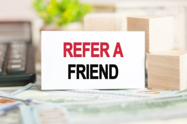 REFER A FriEND, tahta küplerin yakınındaki beyaz kağıt kartlara, hesap makinesine ve banknotlara yazılır. İş ve Finans kavramı