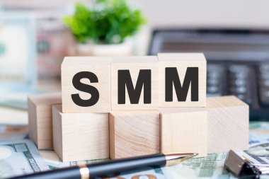 Hesap makinesi ve kelime SMM ile dolar banknotu. Banknotlar ve harfli tahta küpler. Tahta bloklar ve hesap makinesiyle kavram. SMM - Sosyal Medya Pazarlaması