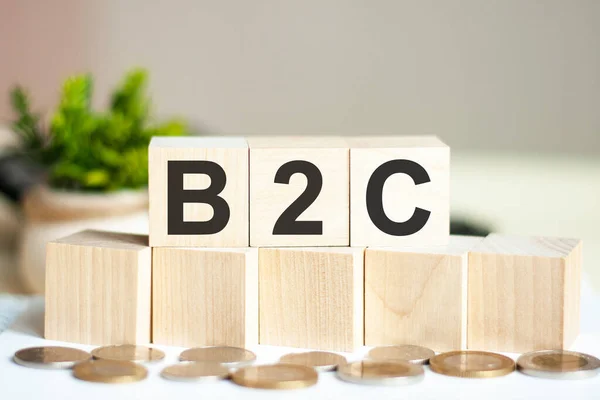 Concept words B2C on wooden blocks on beautiful background. The word B2C on wood cubes with coins on the background. Business concept. B2C - Business-to-consumer
