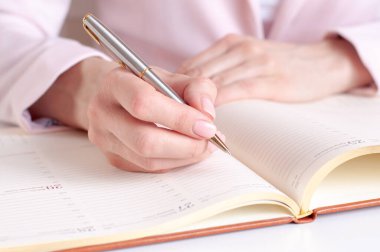 Ahşap masaya beyaz boş bir defter yazan bir kadının yakın plan resmi. Pembe arka plan, seçici odaklanma. İş ve eğitim kavramı.