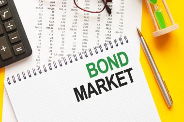 BOND MARKET 'i gösteren metin yazılıyor. Beyaz not kağıdına BOND MARKET yazısı yazmak, yeşil ve siyah harfler, sarı arkaplan. İş konsepti.