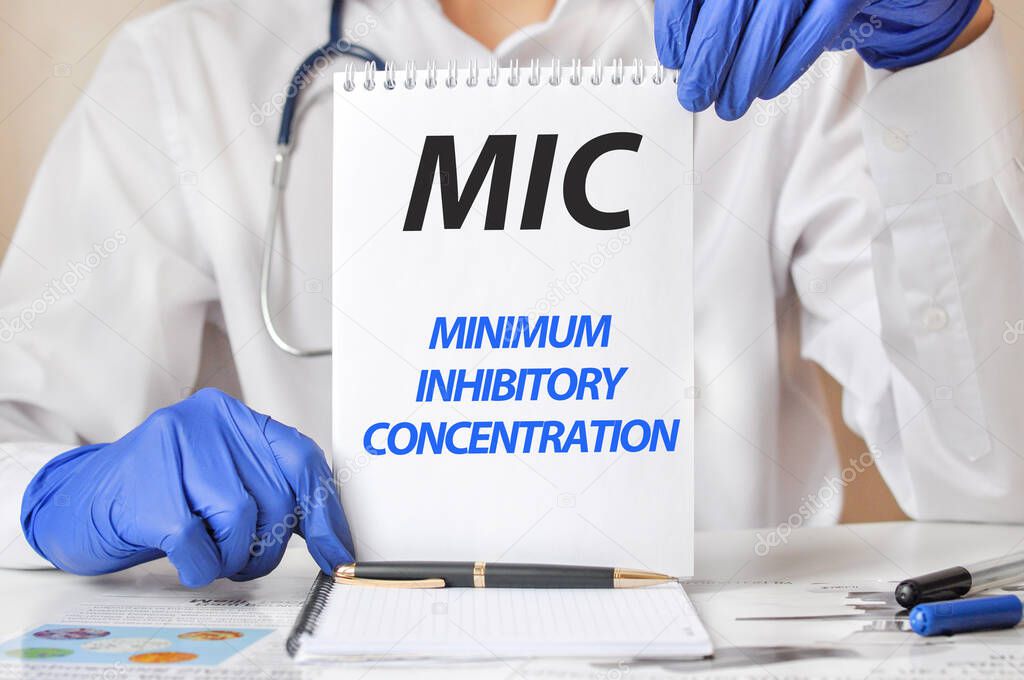 Doctor's hands in blue gloves holding a sheet of paper with text MIC. MIC - short for Minimum Inhibitory Concentration, medical concept.