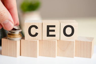 CEO kelimesi tahta küplere yazılmış. Bir adamın eli sikkeleri küpün yüzeyine yerleştirir. Arka planda saksıdaki yeşil bitki. İş ve finans kavramı. CEO - Genel Müdür 'ün kısaltılmışı