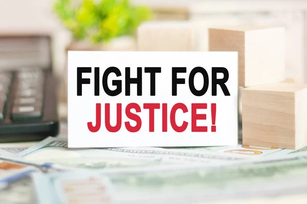 The words FIGHT FOR JUSTICE is written on white paper card near a wooden cubes, banknotes, black calculator and green plant in the background. Business, Financial and Education concept.