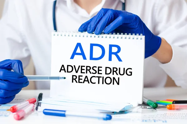 Doctor holding a card with text ADR - short for Adverse Drug Reaction, medical concept. The text is written in blue fnd black letters in a medical journal.