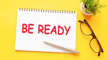 Kelime metni hazır olsun, beyaz kağıt üzerinde, siyah harflerle. Sarı arka planda kalem, bardak ve yeşil çiçek. İş konsepti. Eğitim kavramı