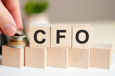 The word CFO written on wood cubes. A man's hand places the coins on the surface of the cube. Business and finance concept. CFO short for Chief Financial Officer