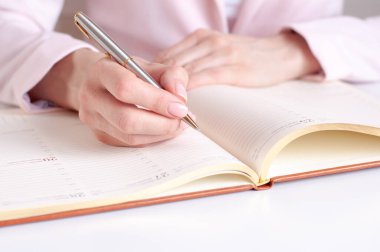 Ahşap masaya beyaz boş bir defter yazan bir kadının yakın plan resmi. Pembe arka plan, seçici odaklanma. İş ve eğitim kavramı.