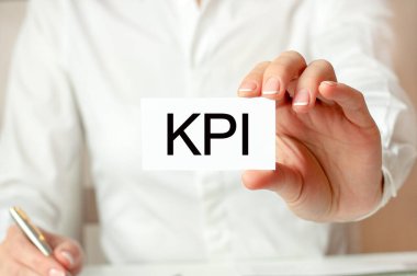 Beyaz gömlekli bir kadın üzerinde KPI yazan bir kağıt parçası tutuyor. KPI - Anahtar Performans Göstergeleri. İş konsepti.