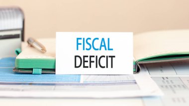 Arka planda FISCAL DEFICIT yazılı beyaz kağıt kart, bir defter, kalem, arka planda damga. İş ve eğitim kavramı.