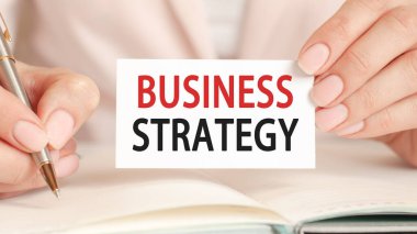 İş kadını defterine gümüş bir kalem ve el sıkışma kartıyla şöyle yazmış: iş stratejisi. Pembe arka plan. İş ve eğitim kavramı.