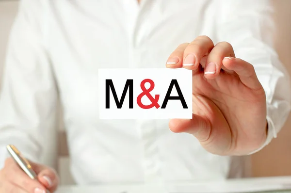 A woman in a white shirt holds a piece of paper with the text: M A. m and A short for Mergers Acquisitions. Business concept for companies.