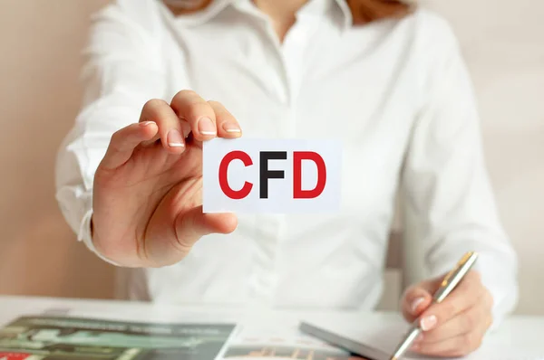 A woman in a white shirt holds a piece of paper with the text: CFD. Business concept for companies. CFD - short for contracts for difference.