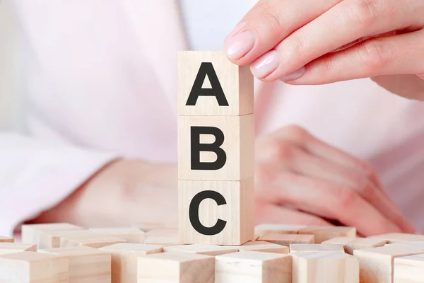 Three wooden cubes with letters ABC, against the background of female hands in pink clothes. Business and economic concept.